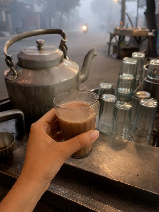 A glass of chai held at a roadside stall on a foggy morning